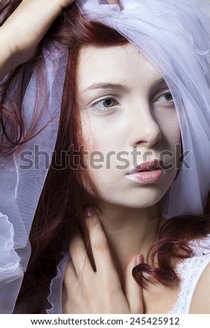 Portrait of red-haired girl with a wedding veil. Hands near face