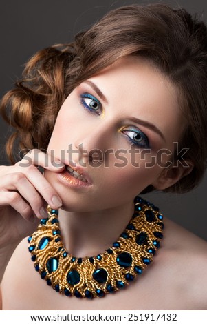 Retro hairstyle. Portrait of brunette Woman with  jewelry. Hand near her lips.On gray background.