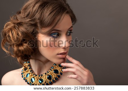 Retro hairstyle. Beautiful Brunette Woman. Fashion portrait with jewerly.On gray background.
