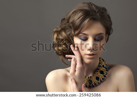 Retro hairstyle. Beautiful Brunette Woman. Fashion portrait with jewerly.On gray background.Hand near her face.