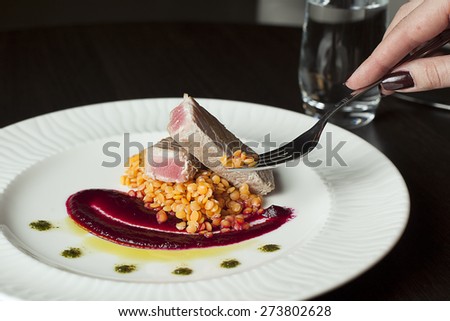 Tuna fillet with lentils and beetroot.Hand holding a fork with food.