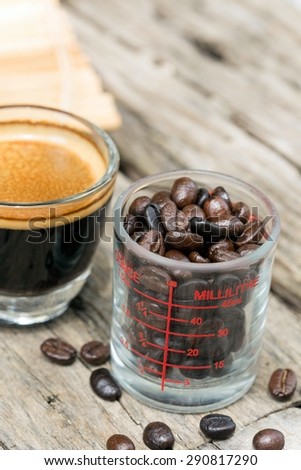 Coffee beans in a glass measuring cup and Espresso coffee cup on the table.