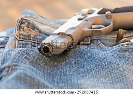 Close-up by focusing on the end of a 9 mm pistol. Rests on a pair of jeans. With the evening light