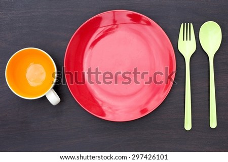 Red empty plate, spoon and fork green plastic. Orange empty coffee cup and placed on a wooden table.