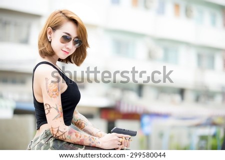 Beautiful Asian woman wearing glasses with a tattoo on the body. Caliber pistol in hand