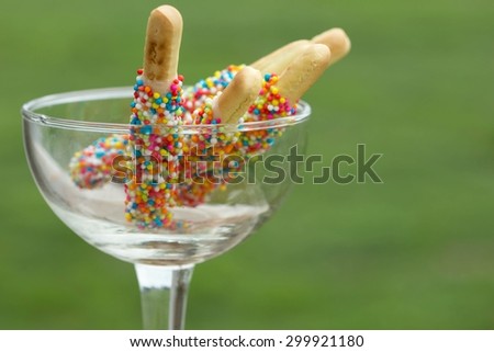 Closeup biscuit stick coated with rainbow in clear glass, natural background afternoon.