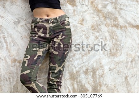 Women wear long Camouflage pants stood against the wall, old plaster.