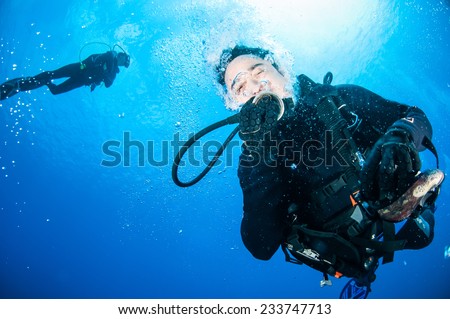 Divers, below the surface in Banda, Indonesia underwater photo. One of the divers is taking off the goggles.