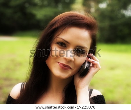 Close-up portrait of a young beautiful girl chatting by a cell-phone during her walk in a park