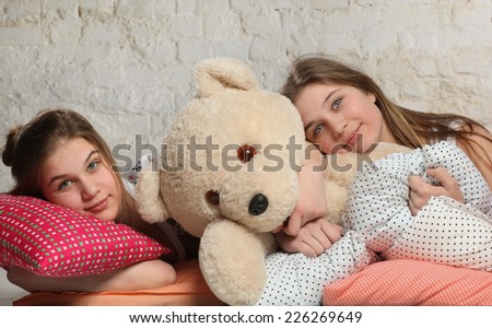 Cute twin sisters going to sleep with pillows and teddy bear