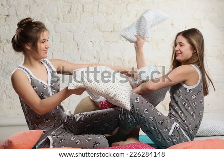 Twin sisters having the battle with the pillows in the bedroom