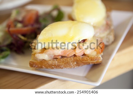 perfect hot Breakfast - baked poached eggs with cheese and smoked salmon on bread with a salad of fresh tomatoes on a white square plate