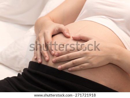 Pregnant Woman holding her hands in a heart shape on her baby bump. Pregnant Belly with fingers Heart symbol