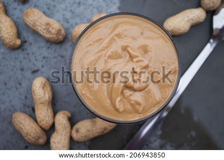 A glass of peanut butter with peanuts in the background