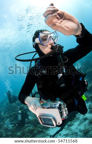 Scuba diver swimming over a tropical coral reef in Bonaire, Netherlands Antilles with her camera checking her dive watch during a safety stop.