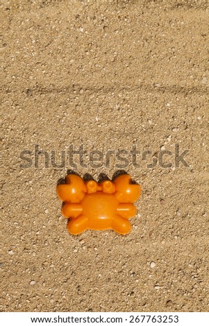 An orange toy crab shape on top of sand in a playground (vertical shot).  The toy is place towards the bottom of the frame allowing for copy-space on top.