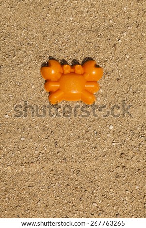 An orange toy crab shape on top of sand in a playground (vertical shot).