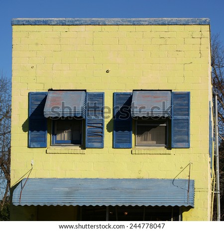 Blue window shutters on a weathered concrete yellow wall with awning
