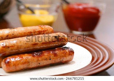 Grilled brats on a stacked on a plate ready to serve with condiments ketchup and mustard and buns ready