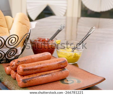 Grilled hot dogs on a stacked on a plate ready to serve with condimaents ketchup and mustard and buns ready