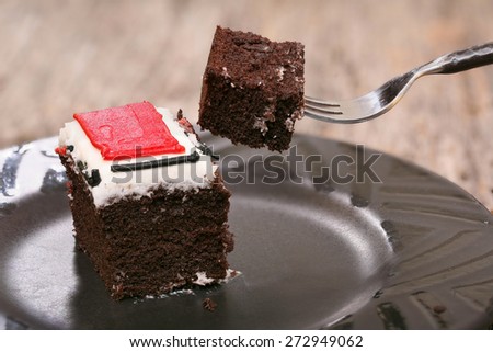 Piece of chocolate cake with colorful frosting close-up and fork with individual bite