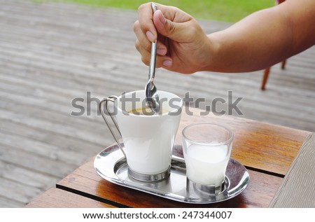 Hand with spoon on Coffee with milk on stainless steel plate