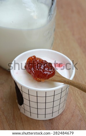 Timber spoon of strawberry jam on milk ice cream cup with milk jar on timber block