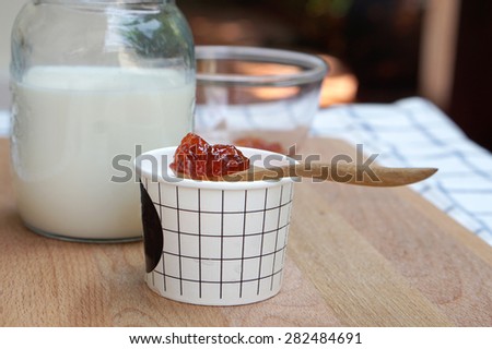Milk ice cream in white cup with Spoon of strawberry jam on top  and milk jar background on timber block