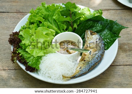 closed up of Thai style fried mackerel fish serving with fresh salad , rice noodle and spicy dressing sauce