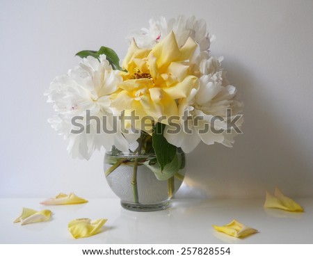 Still life with bouquet of peony flowers and roses in a vase. Floral still life with white peonies and yellow rose and petals. Home decoration with bouquet of flowers.