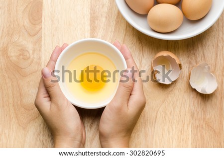 Fresh egg yolk in the bowl are holding by hand on wooden background
