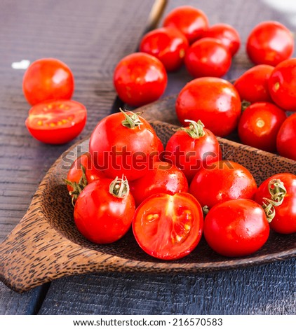 red juicy tomatoes cherry in brown wooden plate on the dark wooden board