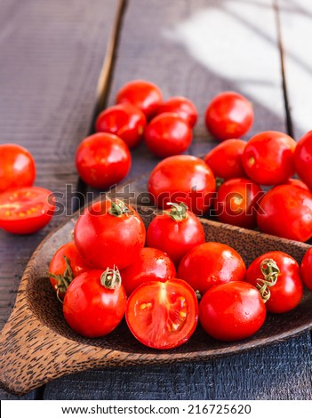 red juicy tomatoes cherry in brown wooden plate on the dark board