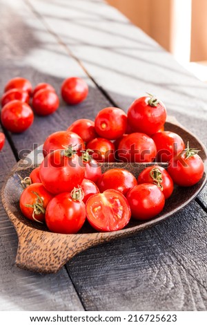 red juicy tomatoes cherry in brown wooden plate on the dark board, vertically