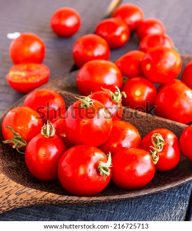 red juicy tomatoes cherry in brown wooden plate on the dark  board, vertically