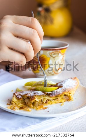 eat apple strudel on a white plate, hands,  fork on a white wooden board
