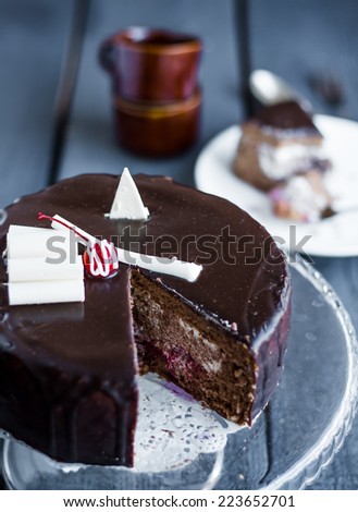 section of chocolate cake with cream and cherry on the stand, on a wooden board