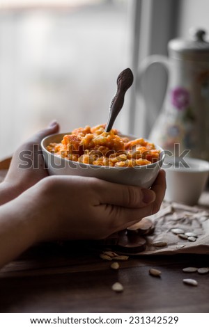 eating pumpkin millet porridge with milk, hands, breakfast on a wooden background
