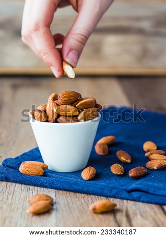 eat nuts, almonds hands of white cup on a wooden board