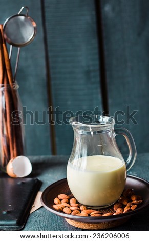 condensed milk in a jug glass, dark almonds on a plate on a wooden board