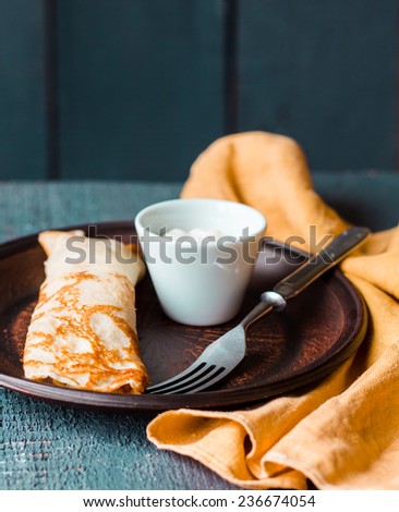 thin pancakes stuffed with sour cream, Slavic cuisine, fork, on dark wooden board
