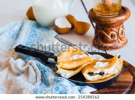 sweet pancakes with cottage cheese, prunes, honey and sour cream, rustic, in a frying pan