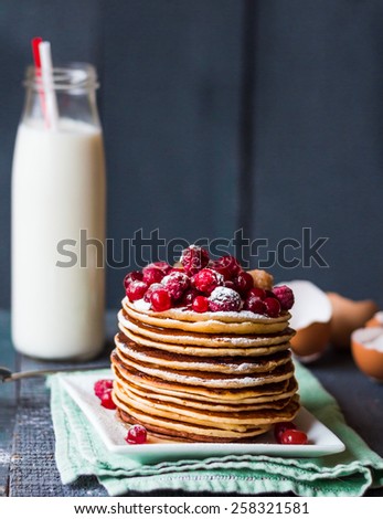 Pancake with cranberries, raspberries, honey and powdered sugar on a blue background
