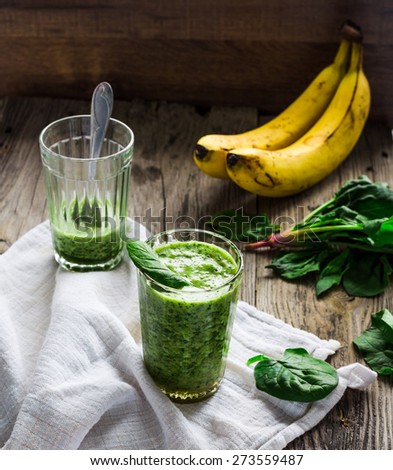 green smoothie with spinach leaves, banana with peanut milk in a glass on a gray wooden background