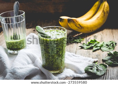 green smoothie with spinach leaves, banana with peanut milk in a glass on a gray wooden background, rustic