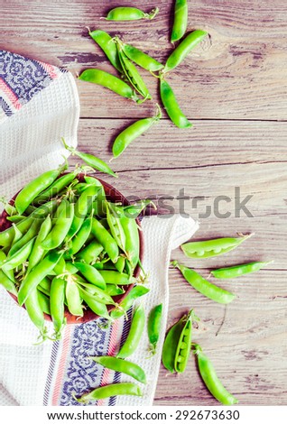 young green peas in the pod, earthenware dish, rustic background, raw,\clean eating, top view