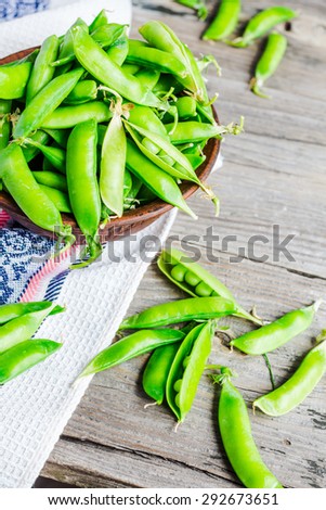 young green peas in the pod, earthenware dish, rustic background, raw,\
clean eating, selective focus