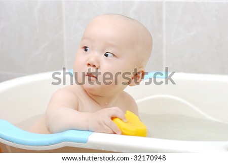Asian baby boy holding  a yellow plastic duck in bath