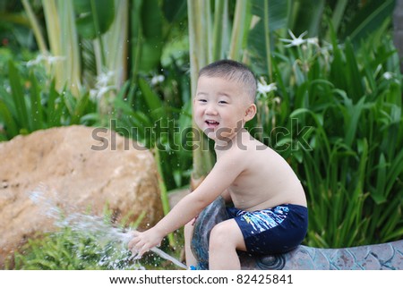 little boy plays with water jet from fish-shape hose outdoors