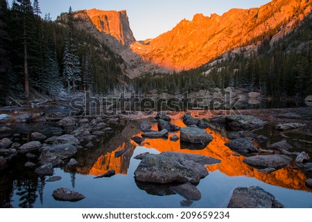 The sun rises over a mirror-like Dream Lake, bathing Hallett Peak in a dramatic red/orange sunrise light.